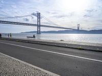 the bicycle rider is standing on the street beside the water, and under the bridge