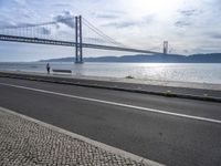 the bicycle rider is standing on the street beside the water, and under the bridge