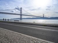 the bicycle rider is standing on the street beside the water, and under the bridge