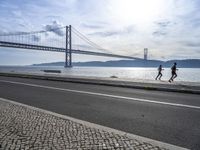 the bicycle rider is standing on the street beside the water, and under the bridge