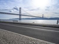 the bicycle rider is standing on the street beside the water, and under the bridge