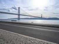 the bicycle rider is standing on the street beside the water, and under the bridge