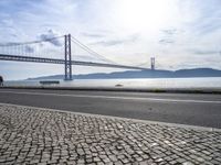 the bicycle rider is standing on the street beside the water, and under the bridge