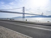 the bicycle rider is standing on the street beside the water, and under the bridge