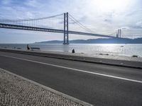 the bicycle rider is standing on the street beside the water, and under the bridge