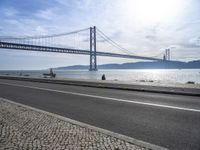 the bicycle rider is standing on the street beside the water, and under the bridge