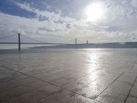 a bridge that is over the water and sky in the background is lit by the sun