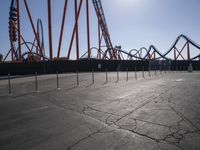 a park has many roller coasters set up for rides with multiple lines of orange painted and orange colored railings