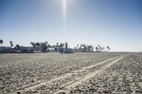 people walk on sand at a beach, near the ocean in the distance is a sky with few cloudless, and blue skies