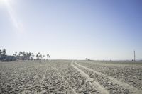 people walk on sand at a beach, near the ocean in the distance is a sky with few cloudless, and blue skies