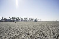 people walk on sand at a beach, near the ocean in the distance is a sky with few cloudless, and blue skies