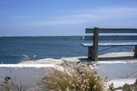 a park bench sitting on a cement wall by the water and sea shore line on a sunny day