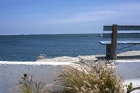 a park bench sitting on a cement wall by the water and sea shore line on a sunny day