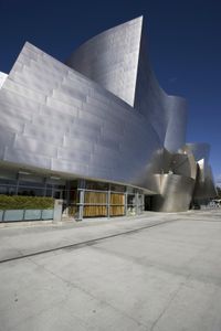 the large silver building has glass panels on the side of it as a building stands in front of a deep blue sky