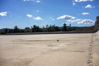 an empty parking lot near the mountains on a sunny day with the sky filled with cloud