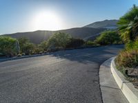 a street with an empty median and mountains in the background with the sun rising behind it