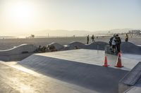 a couple of people on their skate boards in a skate park with orange cones and sand