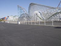 a very tall roller coaster in an empty park surrounded by roller coasters and cranes