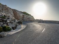 a view from a viewpoint on a winding road, next to rocks and water with the sun and sea in the background