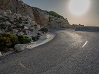 a view from a viewpoint on a winding road, next to rocks and water with the sun and sea in the background