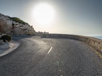 a view from a viewpoint on a winding road, next to rocks and water with the sun and sea in the background