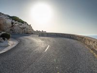 a view from a viewpoint on a winding road, next to rocks and water with the sun and sea in the background