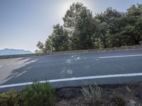 the sun shines behind trees and a long winding highway on a mountain side near trees