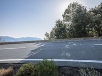 the sun shines behind trees and a long winding highway on a mountain side near trees