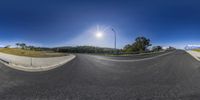 the sun shines over an empty street on a clear day near a hill with grass and trees