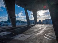 an empty parking lot with a bright sun shining through the clouds above it and a few buildings and the city beyond