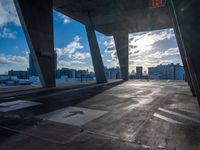 an empty parking lot with a bright sun shining through the clouds above it and a few buildings and the city beyond