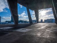 an empty parking lot with a bright sun shining through the clouds above it and a few buildings and the city beyond