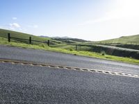 the side view of a motorcycle and a road in front of a fence and grassy hillside