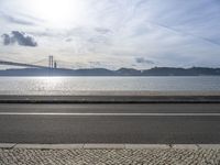 a bus drives down the road near a water view of bridge across the river in a sunny day