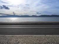 a bus drives down the road near a water view of bridge across the river in a sunny day