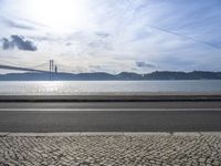 a bus drives down the road near a water view of bridge across the river in a sunny day