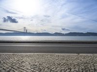 a bus drives down the road near a water view of bridge across the river in a sunny day