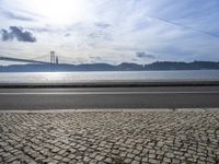 a bus drives down the road near a water view of bridge across the river in a sunny day