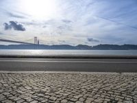 a bus drives down the road near a water view of bridge across the river in a sunny day