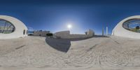 the panoramic image shows a building that has three circular windows and it has sun shining