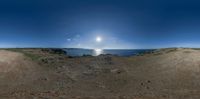 a view of the sun from a dirt hill on the beach with two people on the horizon