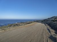 a dirt road beside a shore line with a distant ocean in the background on a sunny day