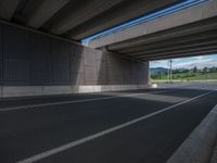 a view from below of an overpass with empty road on right hand side and green area at right end