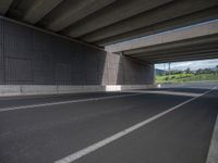 a view from below of an overpass with empty road on right hand side and green area at right end