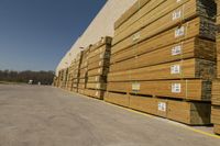 stacks of planks lined up against a large building wall near parking lot with vehicle