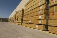 stacks of planks lined up against a large building wall near parking lot with vehicle