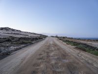 a wide dirt road going into the ocean under a blue sky, with the light on