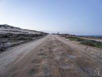 a wide dirt road going into the ocean under a blue sky, with the light on