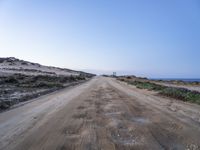 a wide dirt road going into the ocean under a blue sky, with the light on