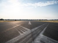 an empty runway with three long lines in the middle of it, and sun on either side